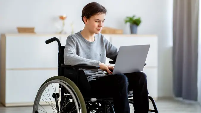 Home schooling concept. Smart disabled teenager in wheelchair using laptop for online education or communication at home stock photo