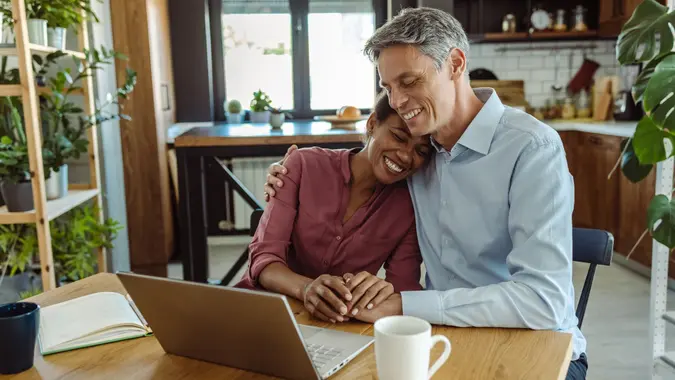 Multi-racial mature couple enjoying home and using laptop stock photo
