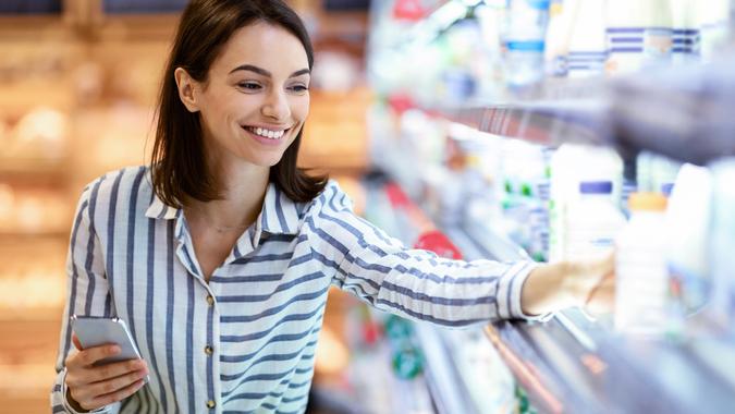 Woman holding smartphone standing in store taking milk stock photo