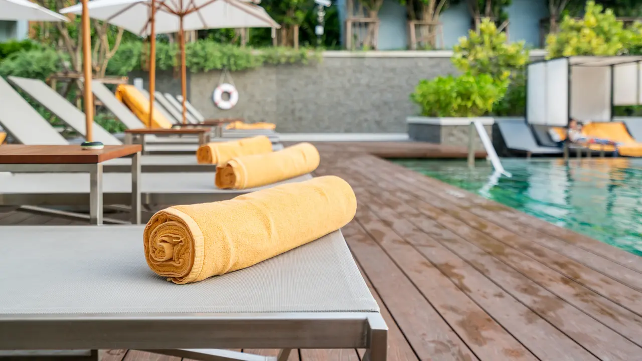 Rolled up orange towel on a sun lounger background of pool in resort or hotel.