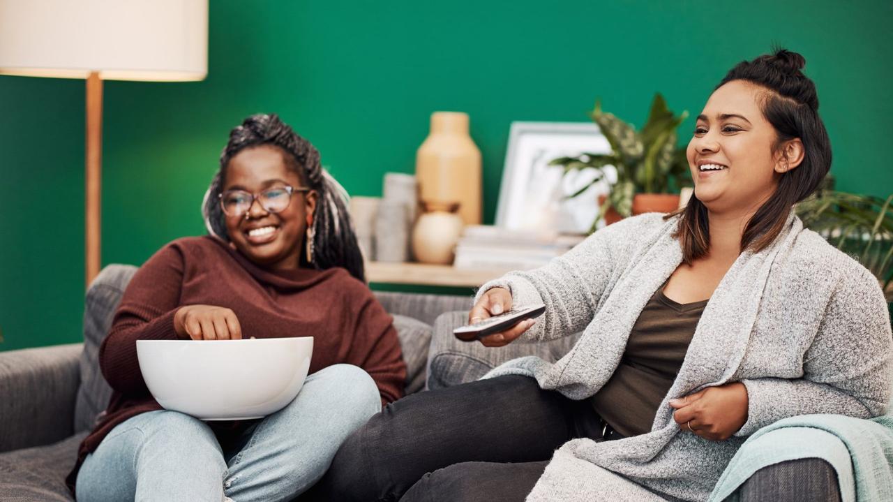 Shot of two young women having popcorn and watching tv together at home.