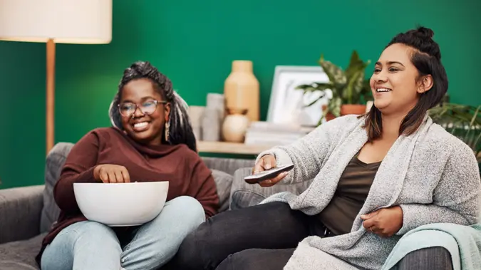 Shot of two young women having popcorn and watching tv together at home.