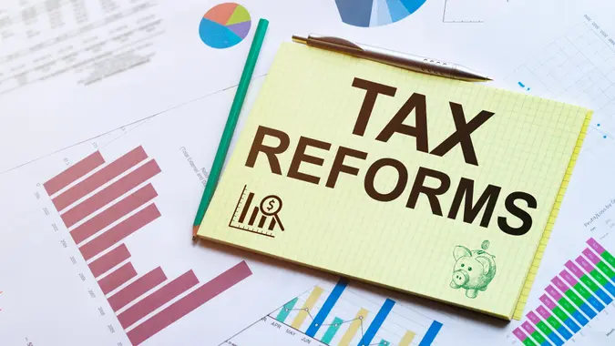 Business reports, blank paper sheet, data tables and charts - directly above view of office table workspace with TAX REFORMS text.