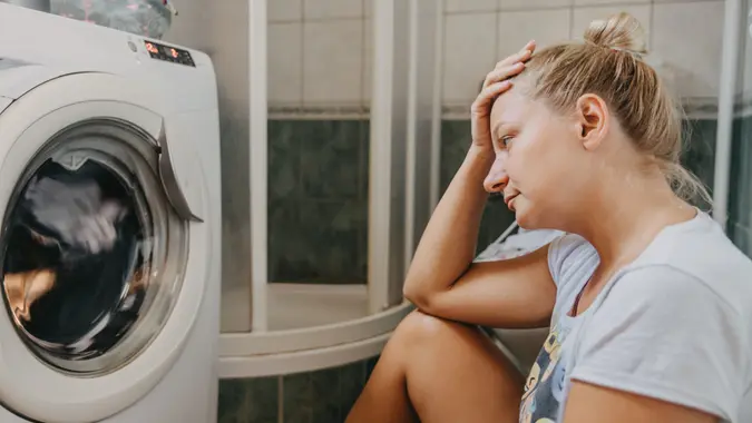 Unhappy woman sitting with head in hands in front of washing machine.