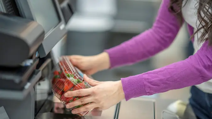Photo of a woman's hand scanning a box of strawberries at a grocery store self-checkout.