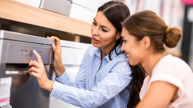 Saleswoman talking to a female customer in front of a dishwasher that she wants to buy for her new apartment.