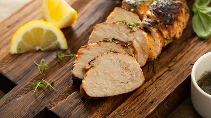 Balsamic grilled chicken breast with fresh herbs sliced on a rustic wooden board.