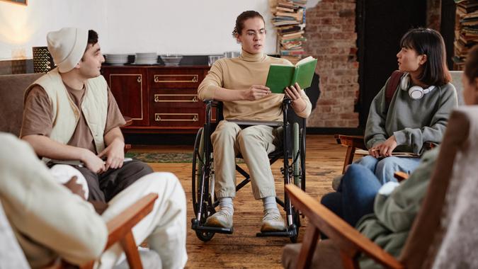 Teenage boy with disability reading a book for group of students during reading classes in the classroom.