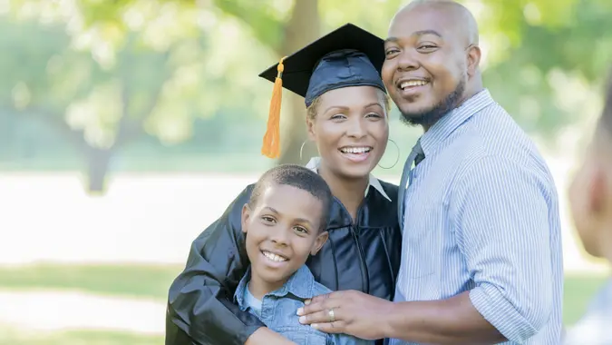 Proud college graduate smiles after graduation with her husband and elementary age son.