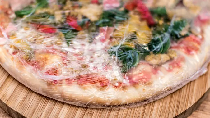 Frozen pizza still in plastic wrap.