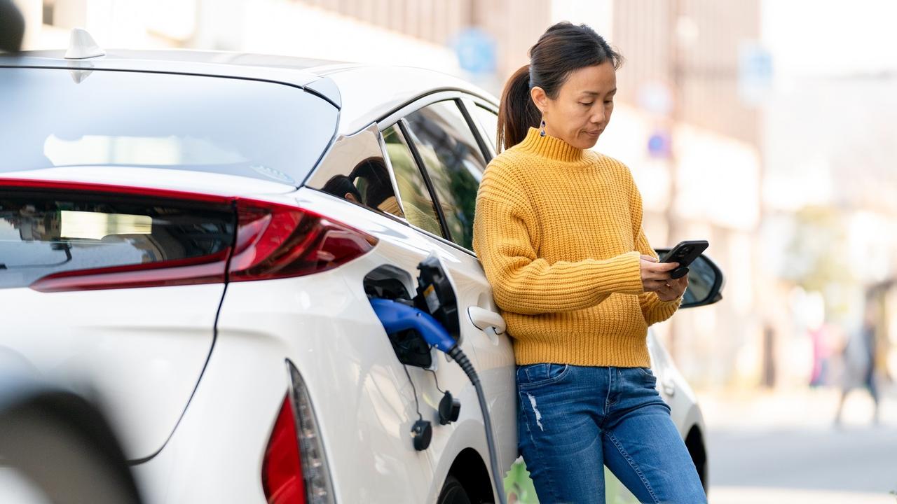 Woman charging electric car while using mobile phone stock photo