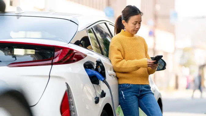 Woman charging electric car while using mobile phone stock photo