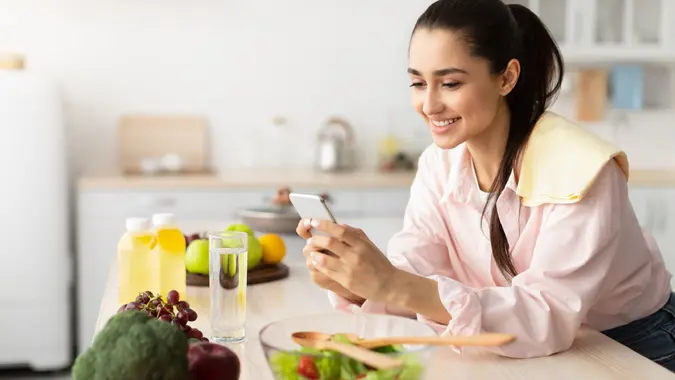Portrait of smiling young woman using cellphone in kitchen stock photo