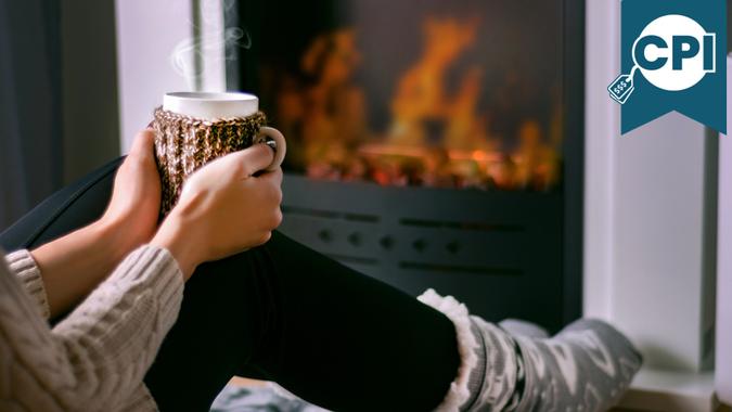 Young girl sitting in front of the fireplace and holding cup of tea in hand on legs and warming.
