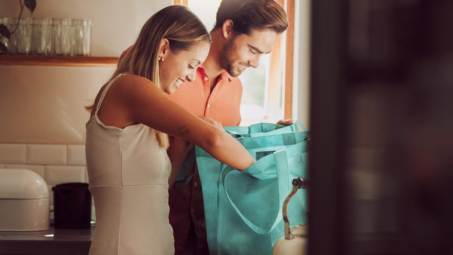 Couple home after grocery shopping at supermarket store. Retail consumer, sustainable shopper and young people unpacking and checking food products, goods and groceries from reusable bag in a kitchen stock photo