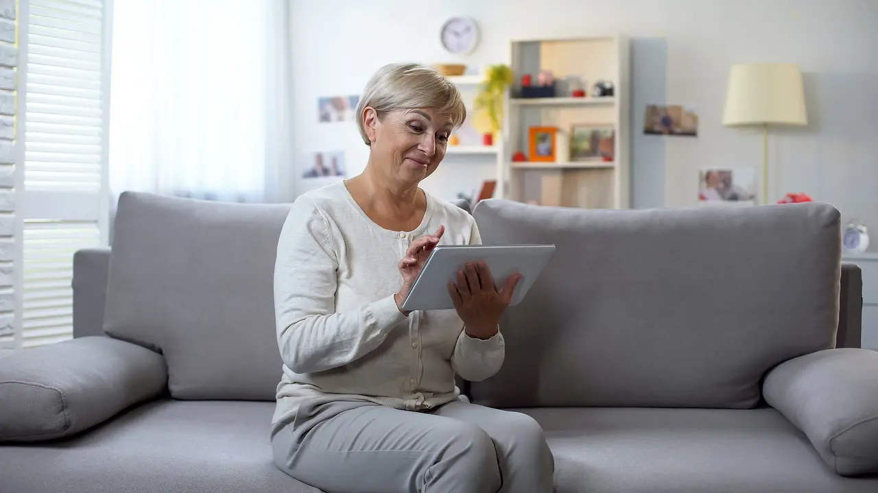 Happy aged woman watching photos on tablet and smiling, spending free time.