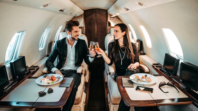Rich couple toasting with glasses of champagne while eating appetizers on board a private jet.