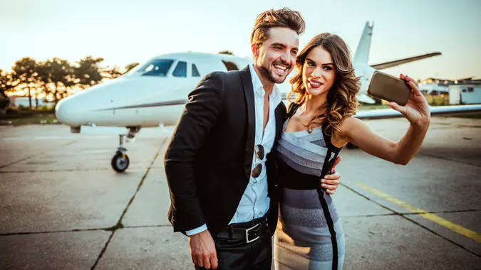 A rich couple poses for a picture in front of their private jet.