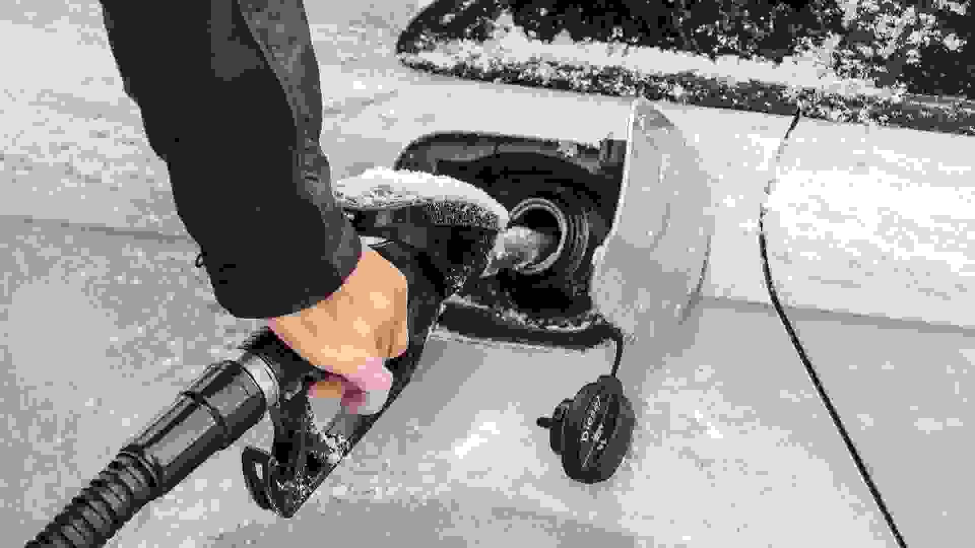 Detail on man's hand holding fuel nozzle, filling gas tank of car covered with snow in winter.