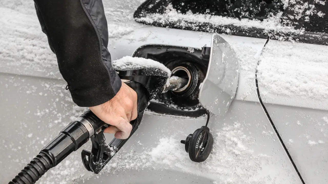 Detail on man's hand holding fuel nozzle, filling gas tank of car covered with snow in winter.