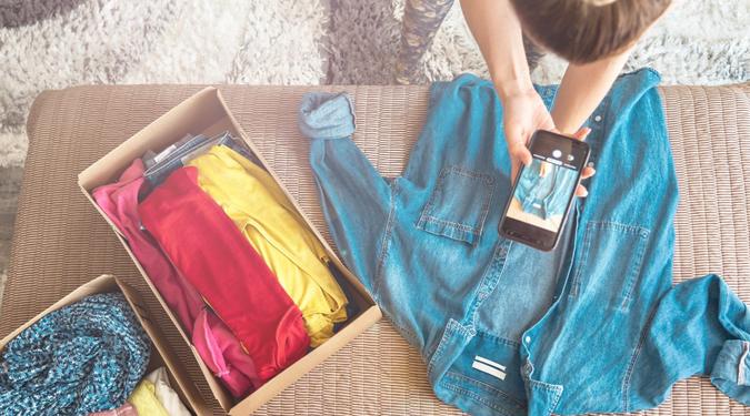 Woman taking photo of denim shirt on smartphone to sell it on internet shop.