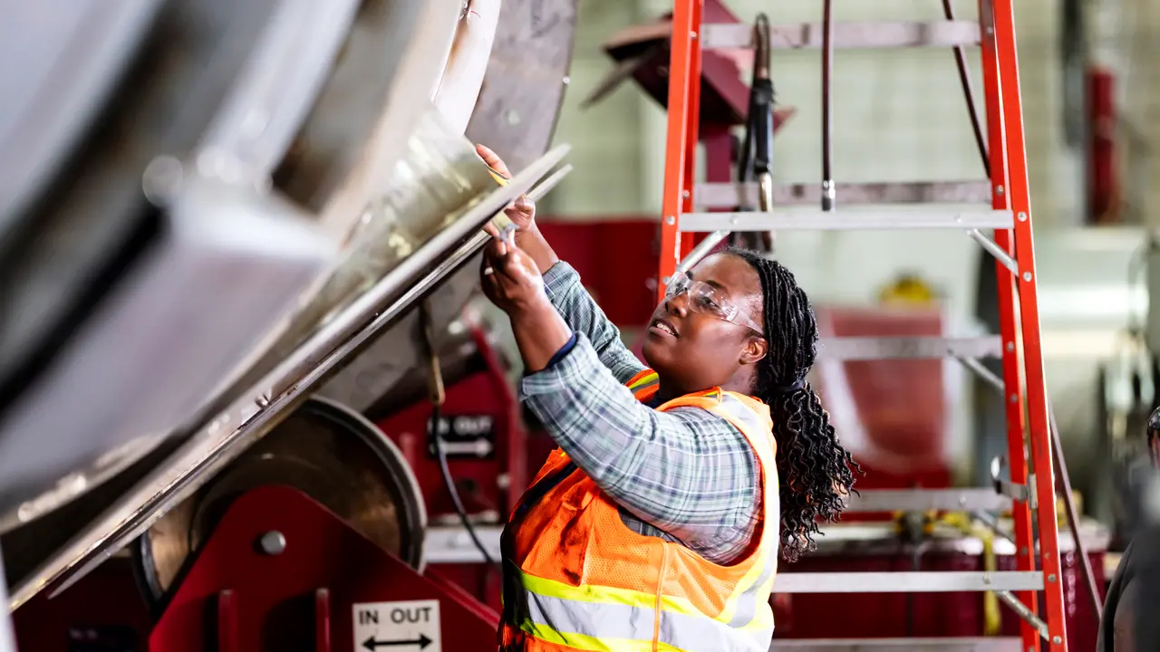 A mature African-American woman working in a metal fabrication shop.