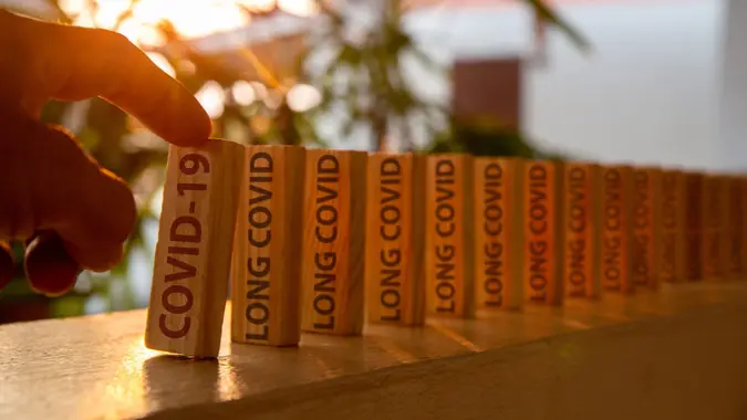 Hand poked on a row of wooden dominoes, with the words "COVID19" on the first piece and the words "LONG COVID" on subsequent pieces.