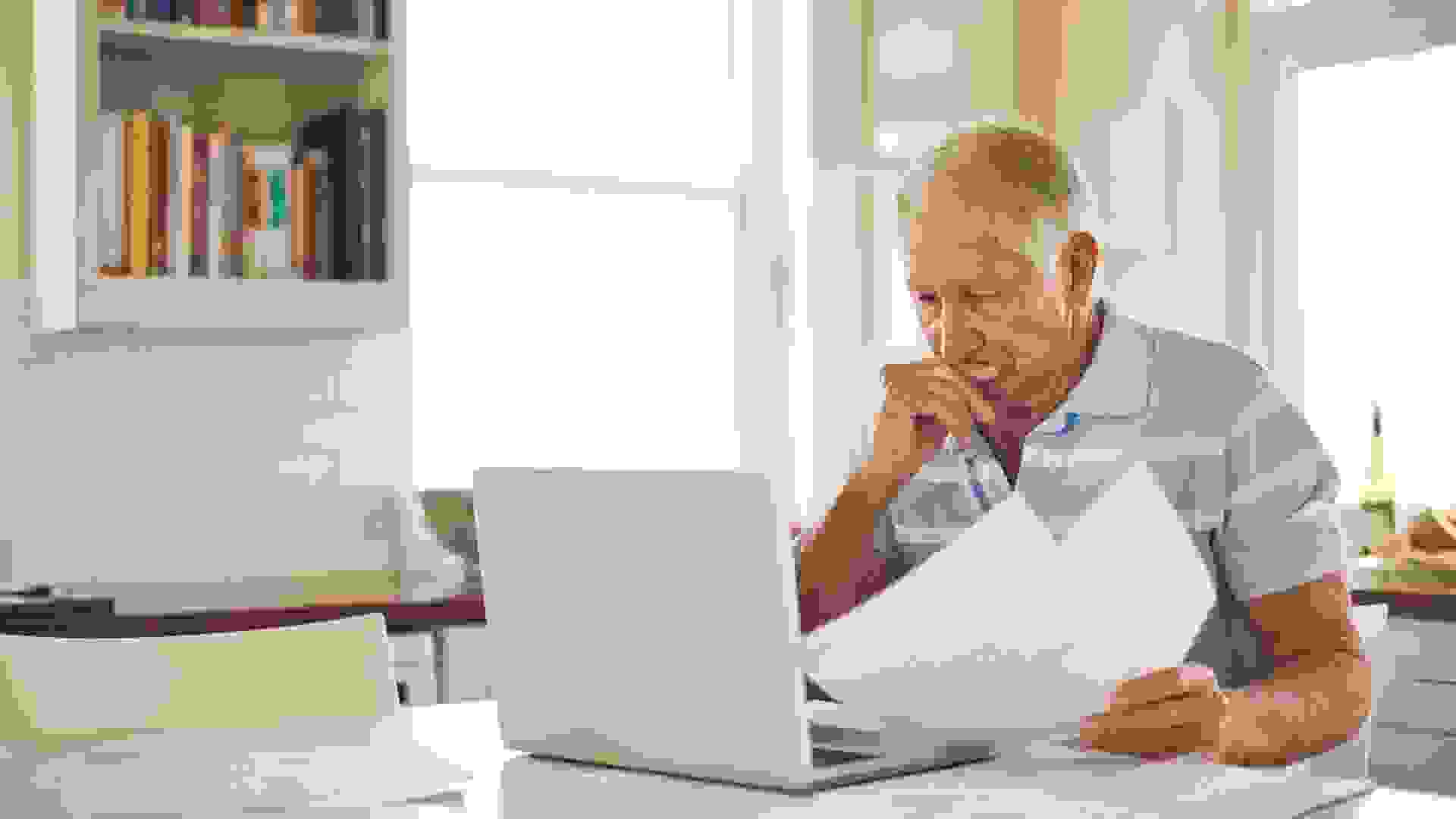 Shot of a senior man looking stressed while doing the household finances on a laptop in his kitchen.