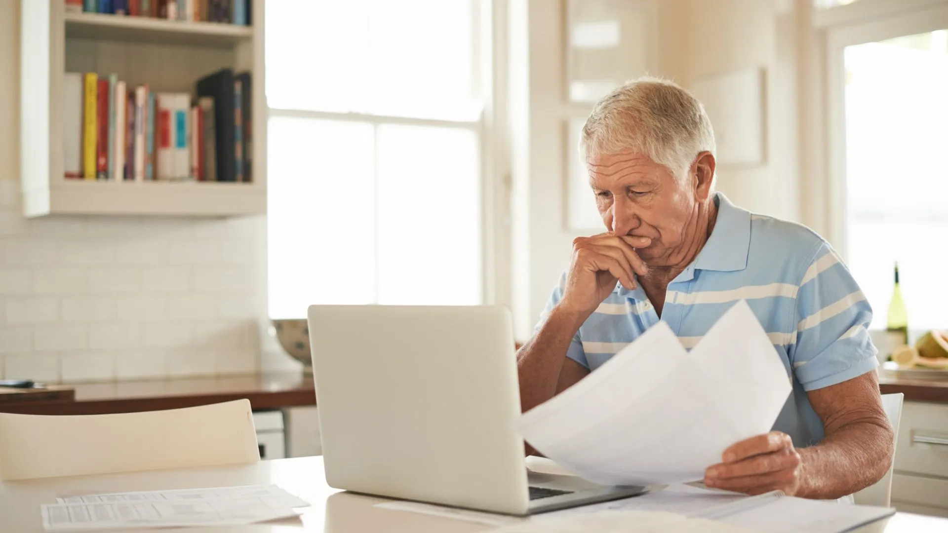 在厨房用笔记本电脑处理家庭财务时，一位老人看起来很紧张。