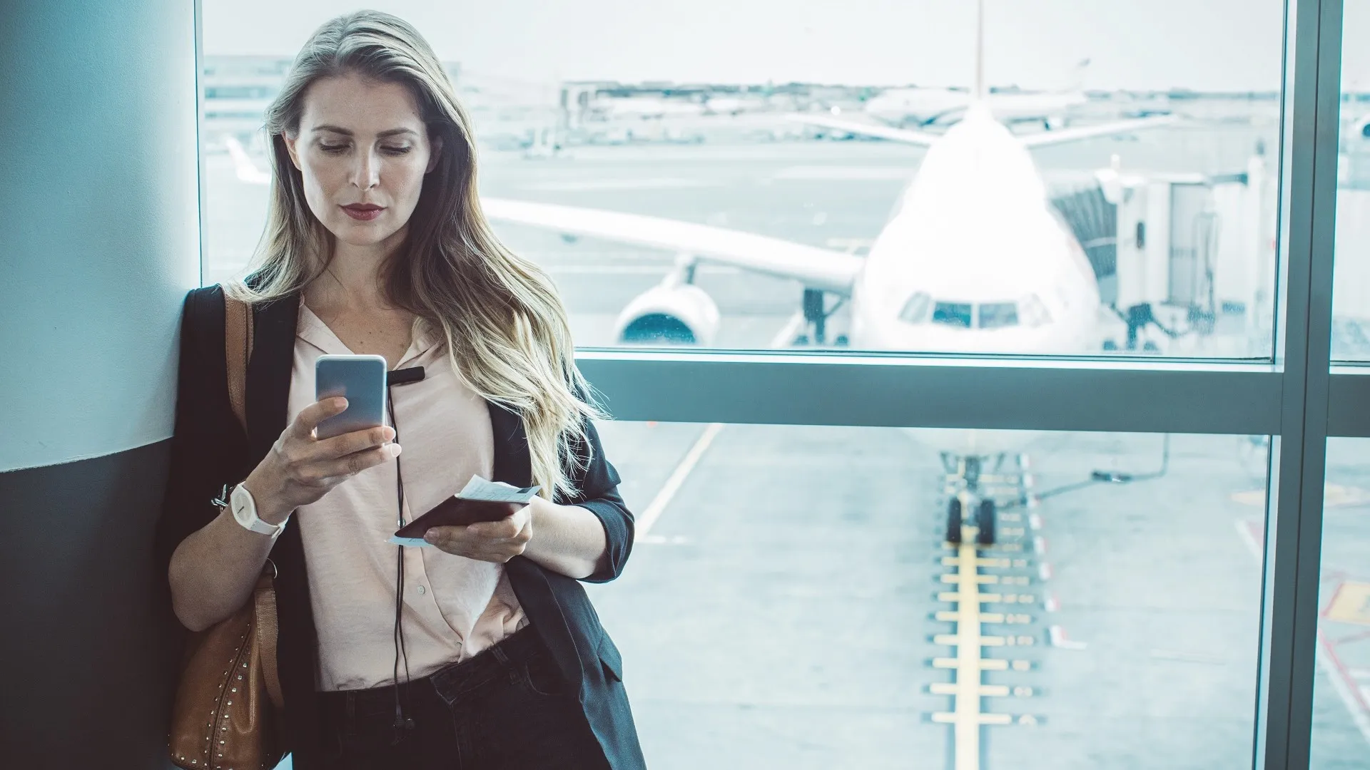 A woman stands in an airport terminal and checks her phone.