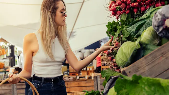 Blond young woman with basket buying radish at market stock photo