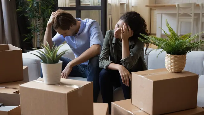 Unhappy frustrated couple sitting on couch with cardboard boxes, eviction stock photo