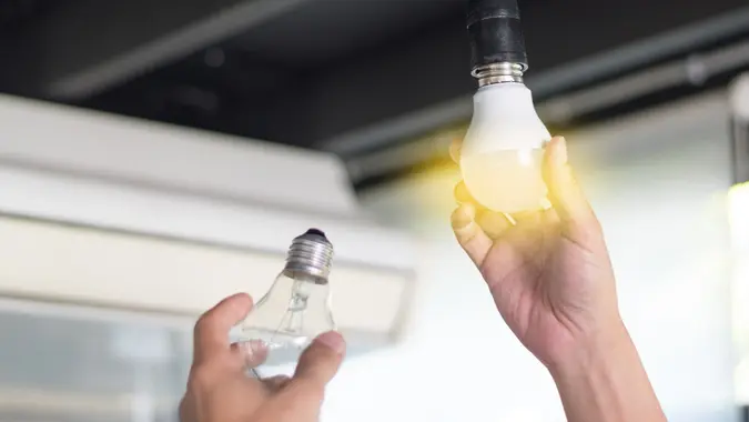 Power saving concept. Asia man changing compact-fluorescent (CFL) bulbs with new LED light bulb. stock photo