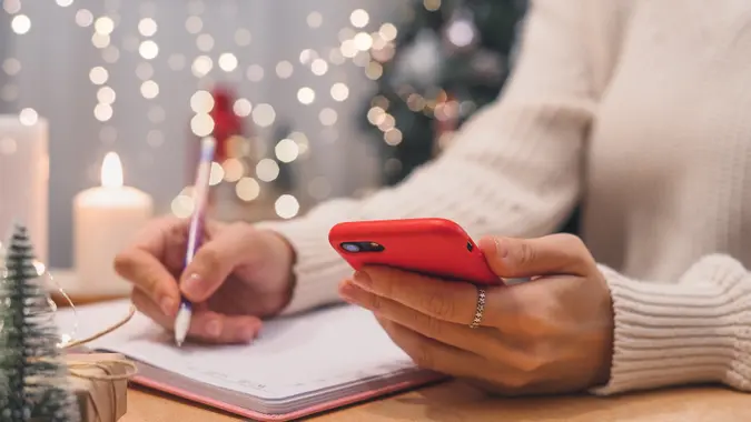 Woman hands with pen and mobile phone writing christmas wish list, goals. stock photo