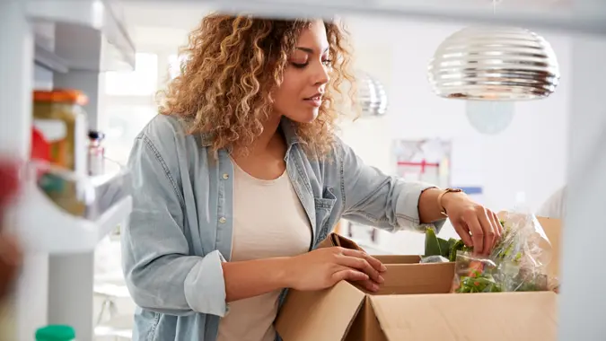 View Looking Out From Inside Of Refrigerator As Woman Unpacks Online Home Food Delivery.