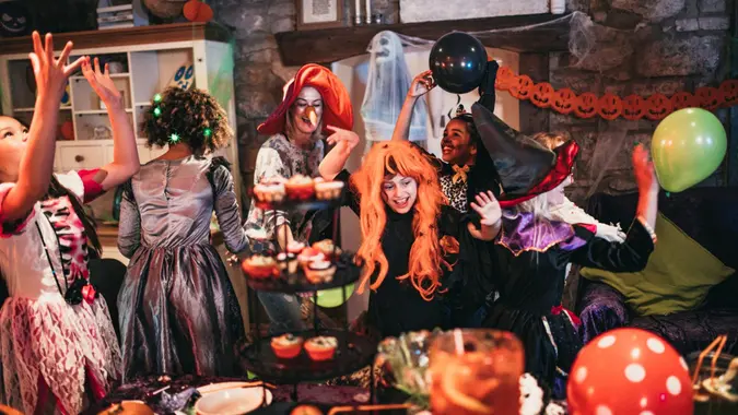 Group of young friends dressed in costumes dancing and playing together at a Halloween party.