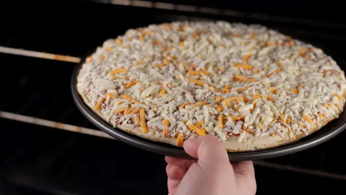 Putting frozen cheese pizza into the oven to bake.