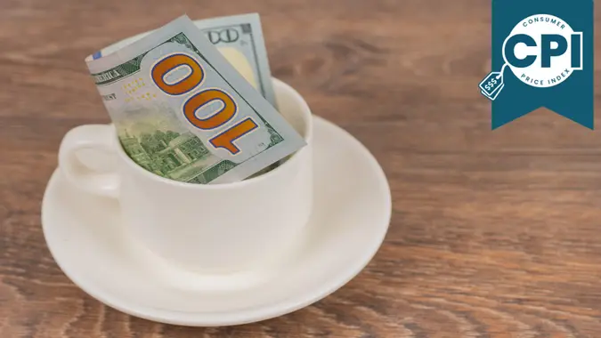 100 dollars banknote in white coffee cup on wooden table, tips or expensive service concept.