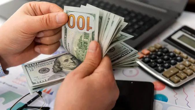 Businessman counting hundreds of dollars at his table.