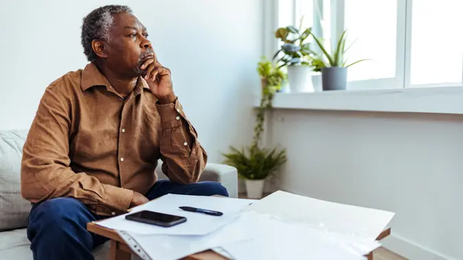 Depressed Senior Adult Man With Stacks of Papers and Envelopes.