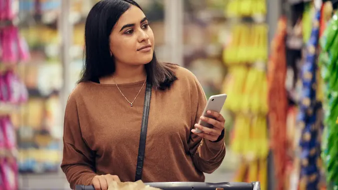 Shot of a woman using her smartphone while doing her grocery shop stock photo