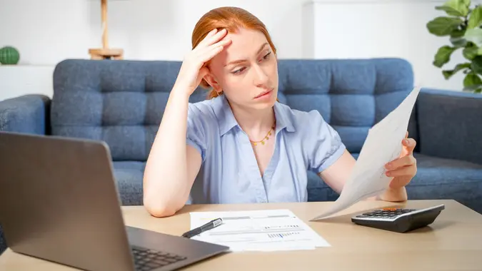 A woman looks stressed after looking a paperwork while sitting at her desk at home.