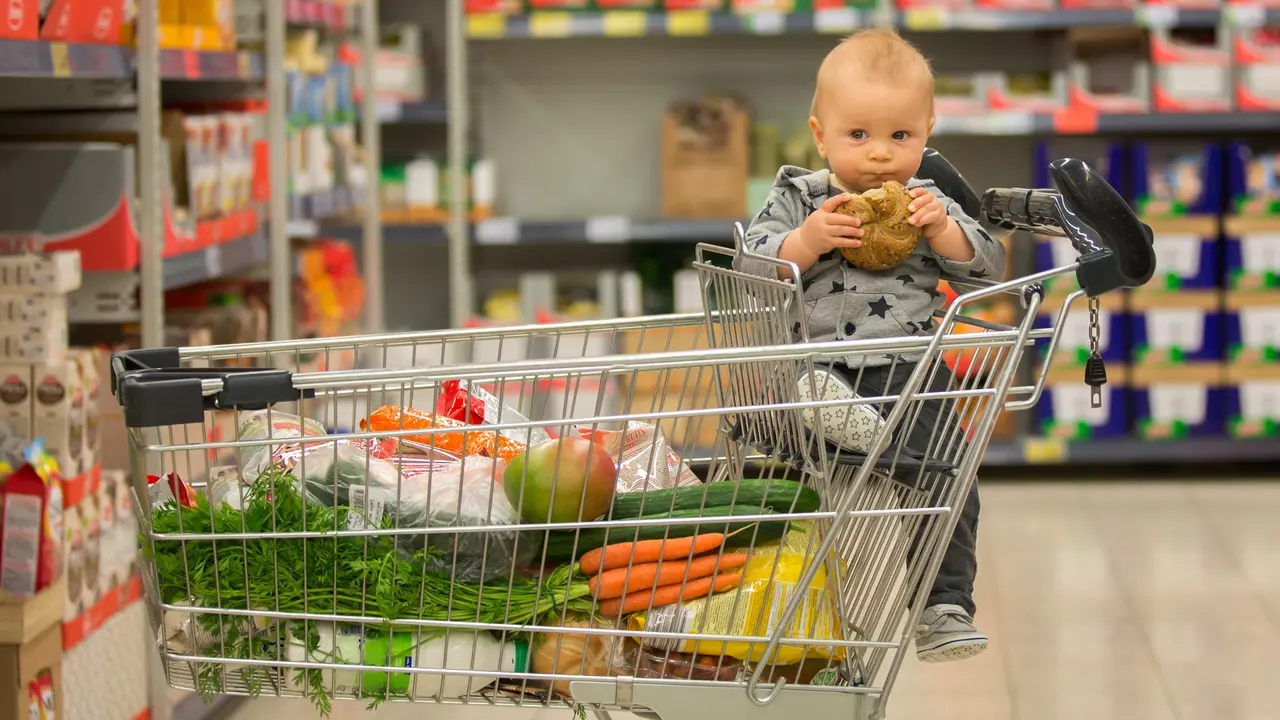 Toddler baby boy, sitting in a shopping cart in grocery store, smiling and eating bread stock photo