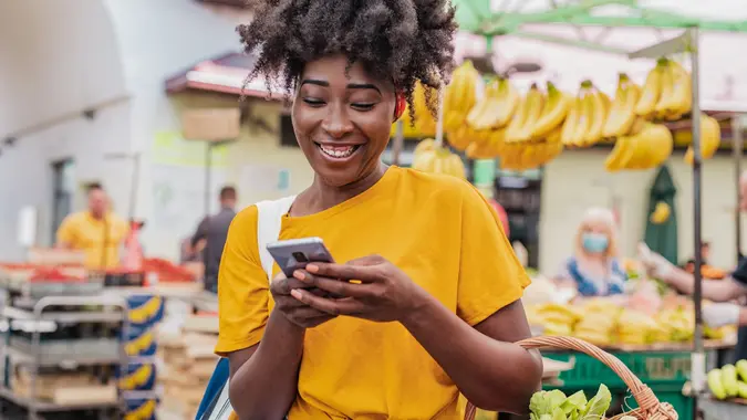 Young African woman holding a shopping basket full of groceries and using mobile phone stock photo