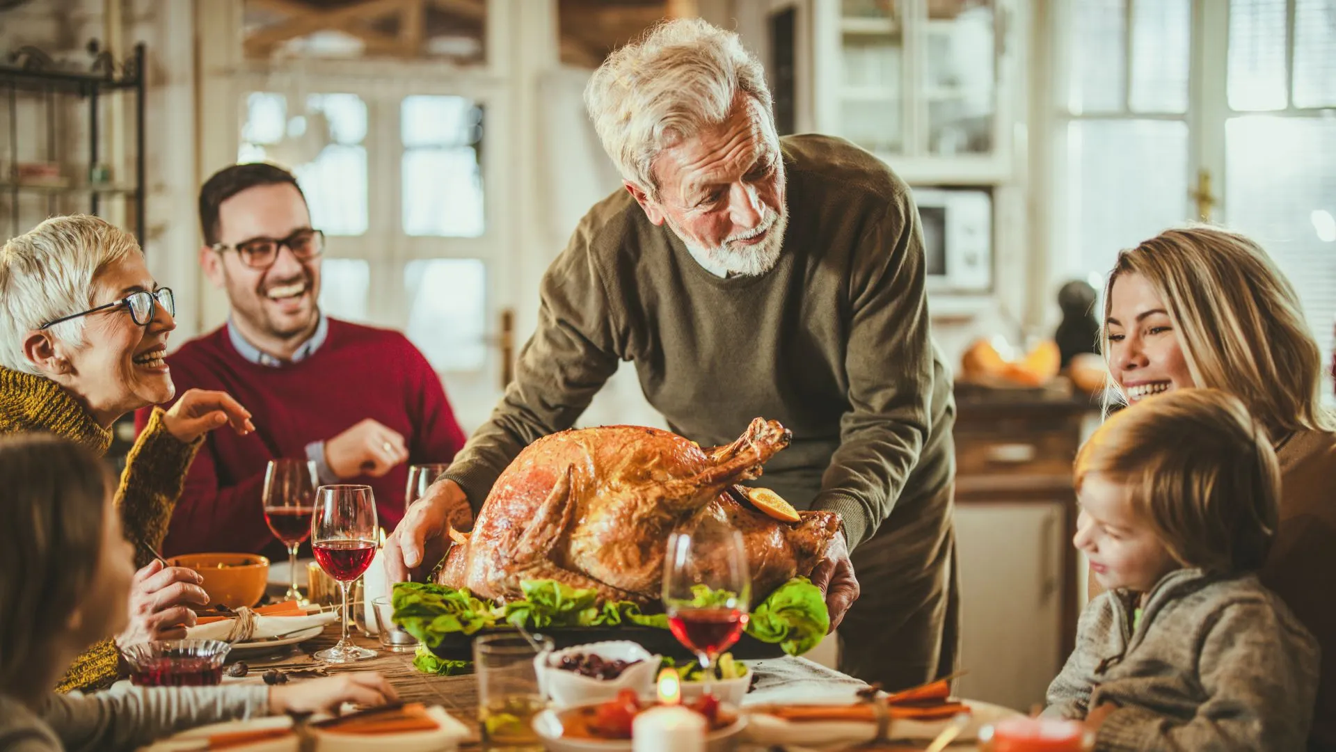 一个快乐的成熟男人一边把感恩节火鸡端上桌，一边和他的孙子说话。