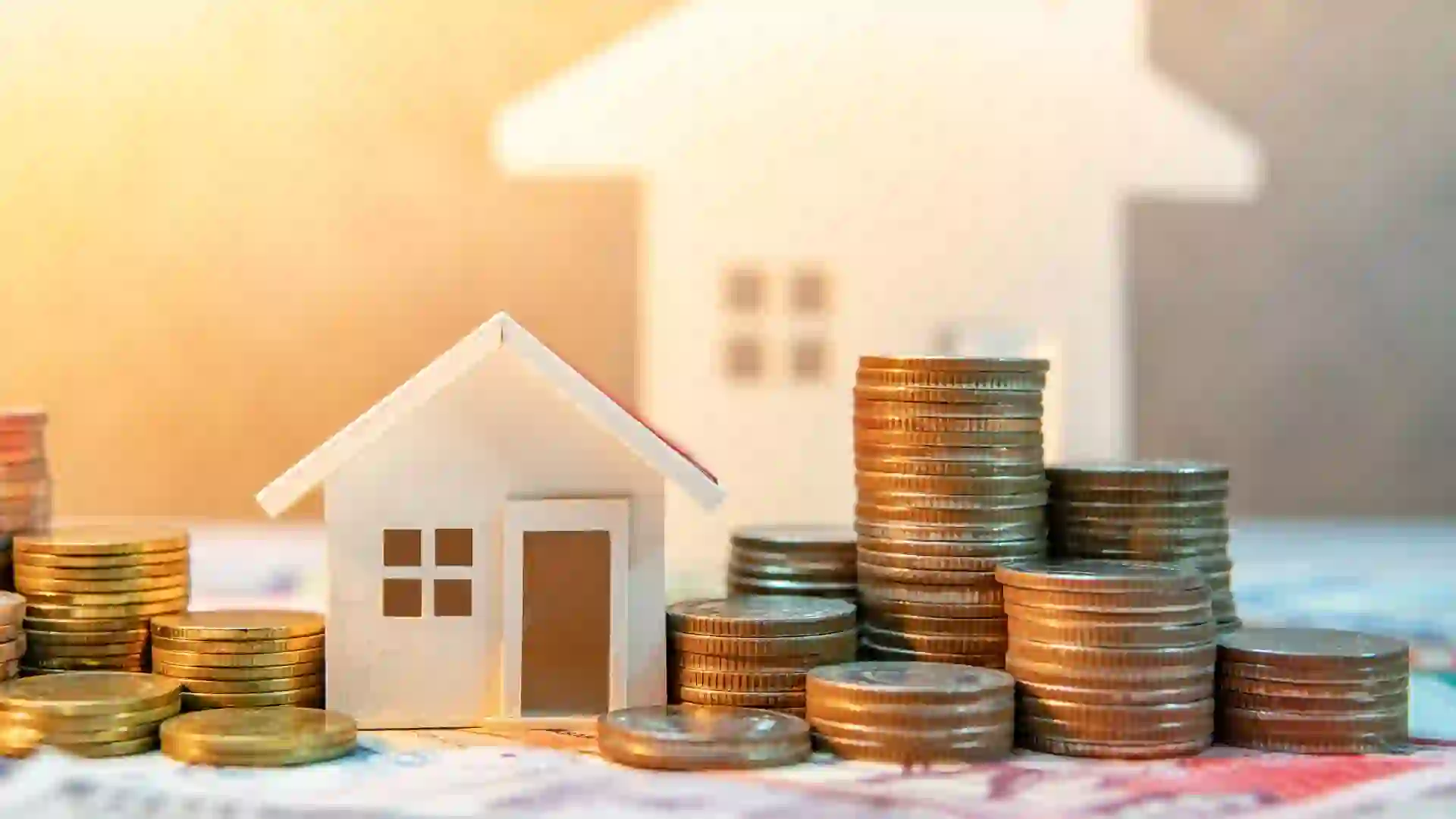 Two small houses sitting on a table with coins stacked up all around them