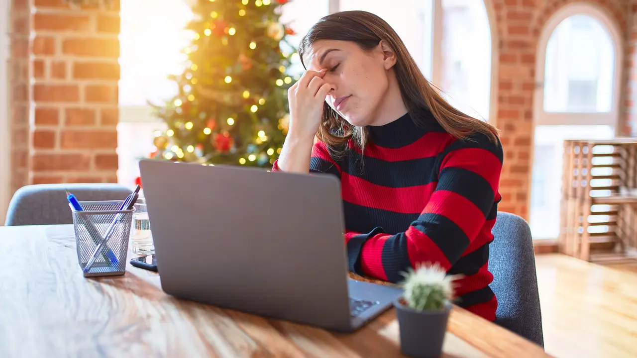 Beautiful woman sitting at the table working with laptop at home around christmas tree tired rubbing nose and eyes feeling fatigue and headache. Stress and frustration concept. stock photo