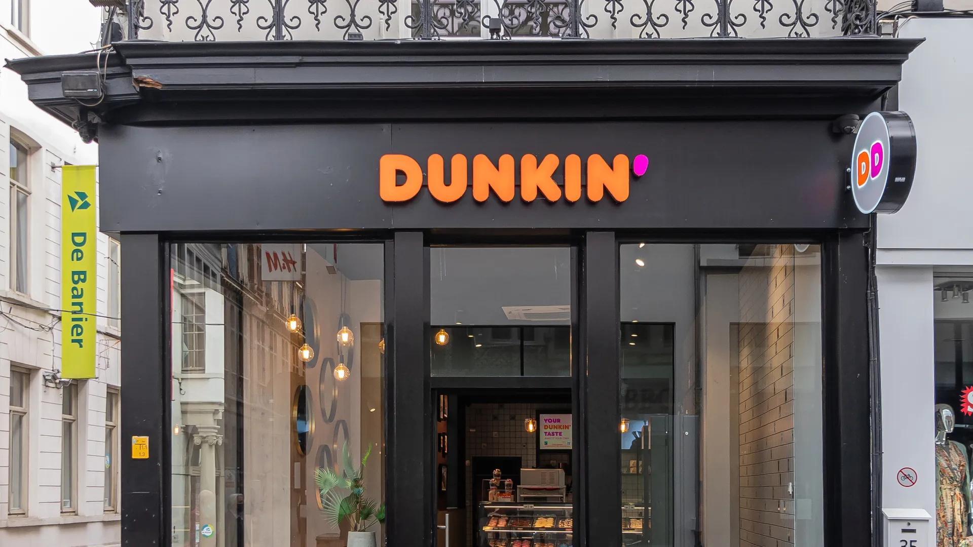 Gent, Flanders, Belgium - July 30, 2021: Dunkin Donuts store black and window facade on corner showing display inside and advertising as DD.