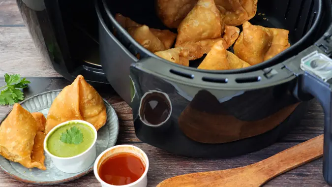 Stock photo showing samosas stuffed with spiced potato, peas and meat in air fryer.