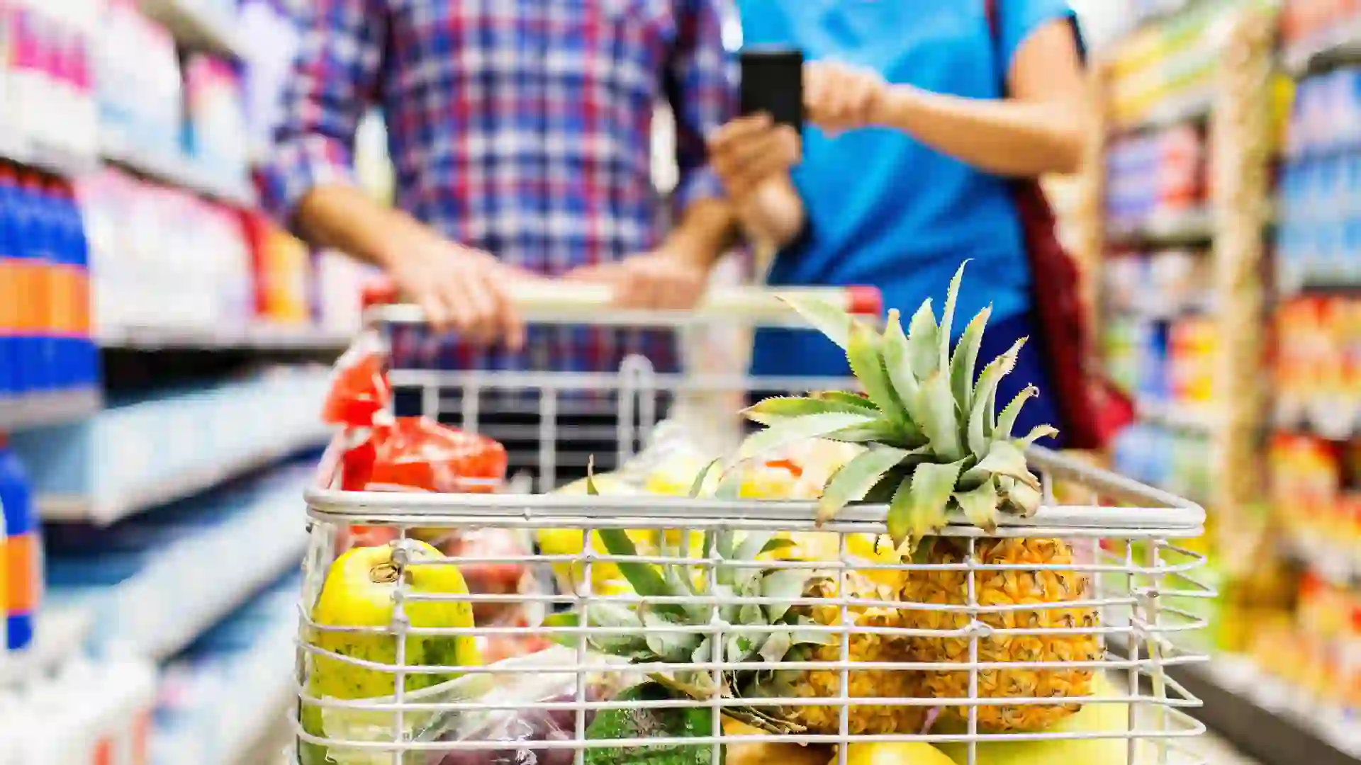 Close-up of fruits in shopping cart with couple using smart phone at grocery store.